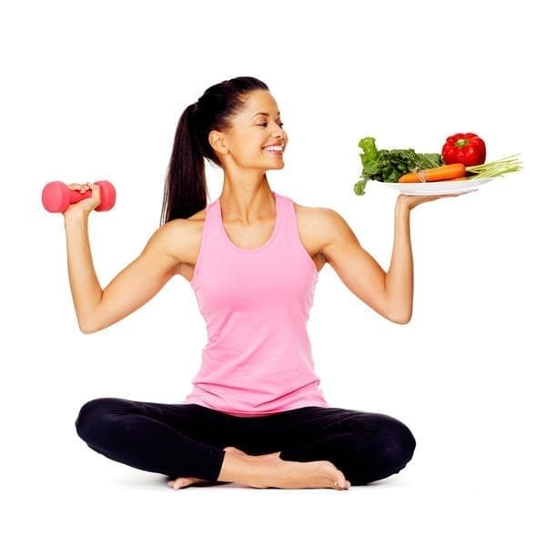 A young woman holding dumbbell and fresh vegetables in her hands.