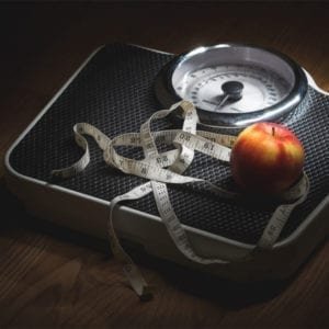 A weighing scale with measuring tape and apple, symbolizing health and wellness.